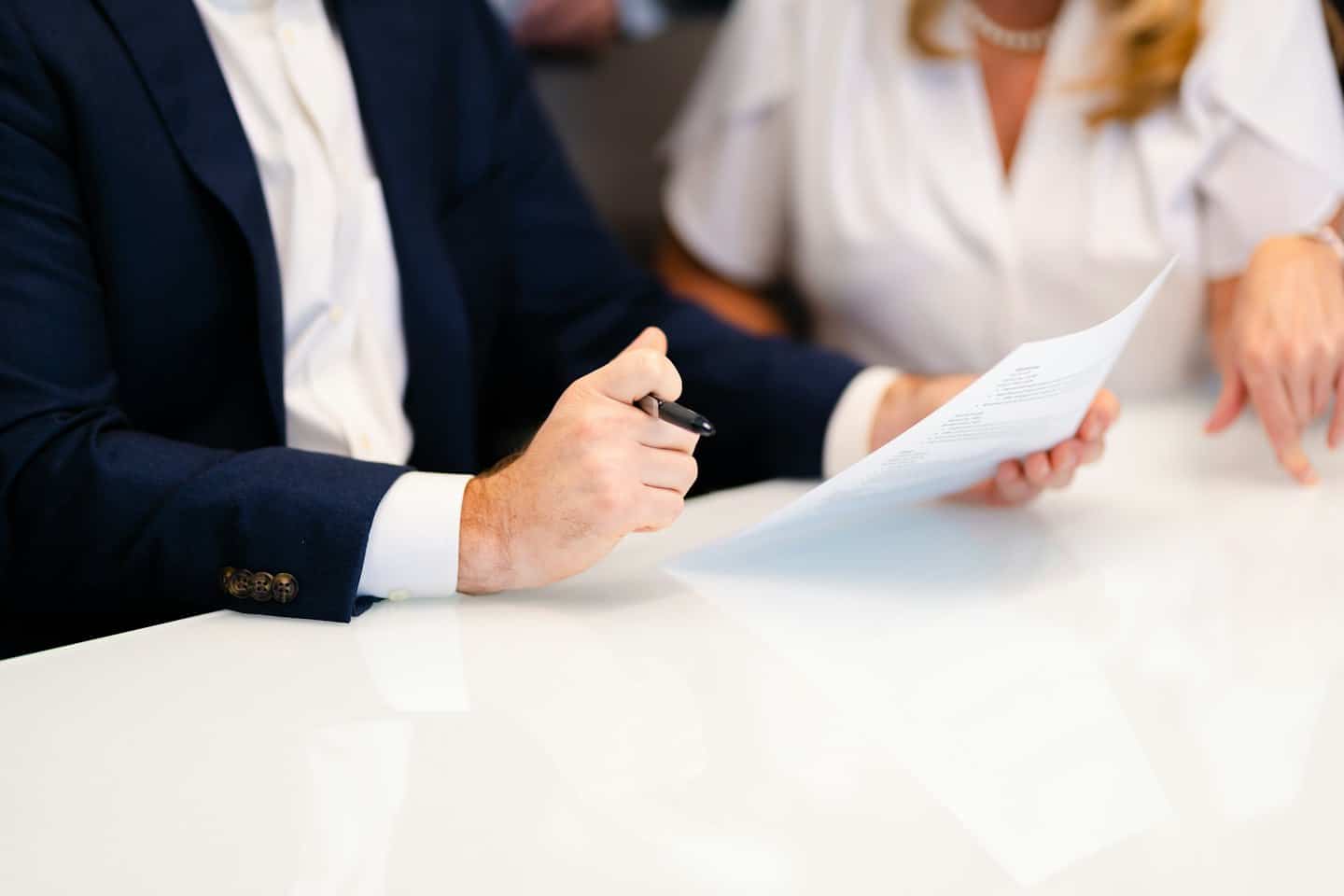 Man and woman reviewing document at white table.